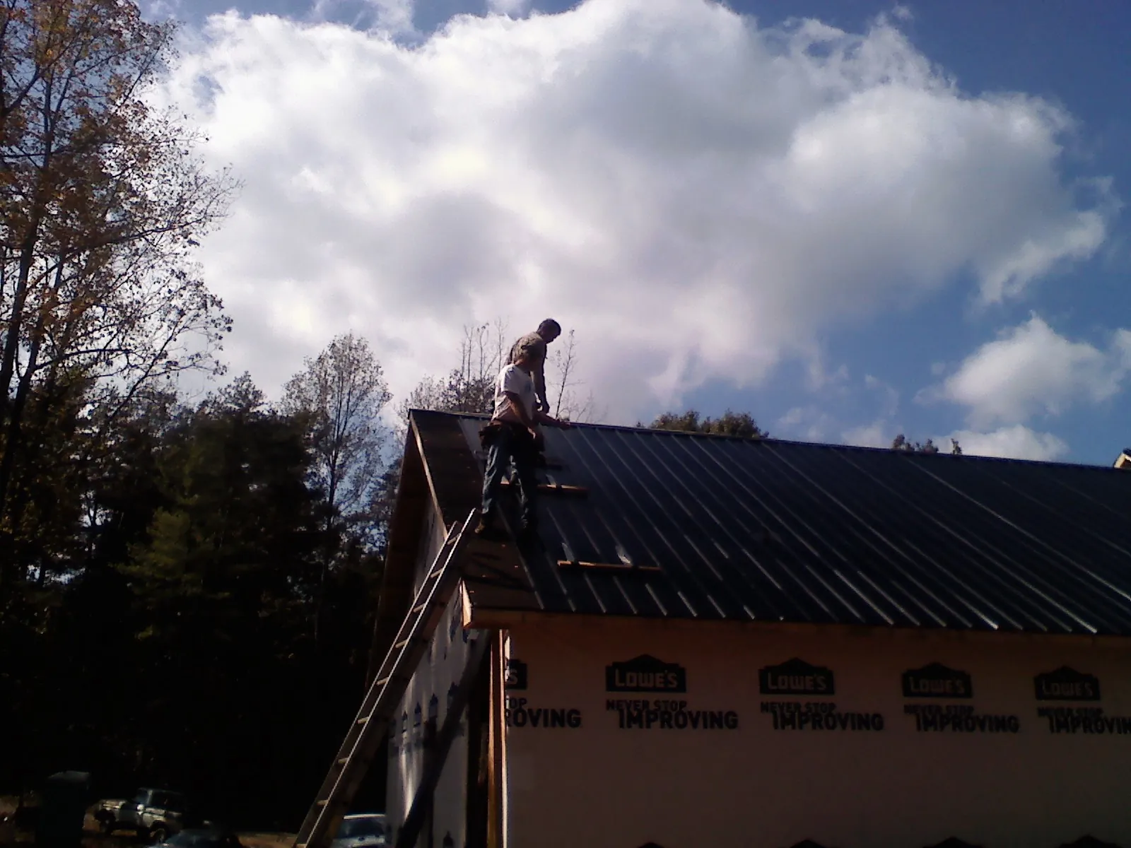 Roofer fastening dark metal panels high against a cloudy sky, from a Roof Inspection job in Folsom